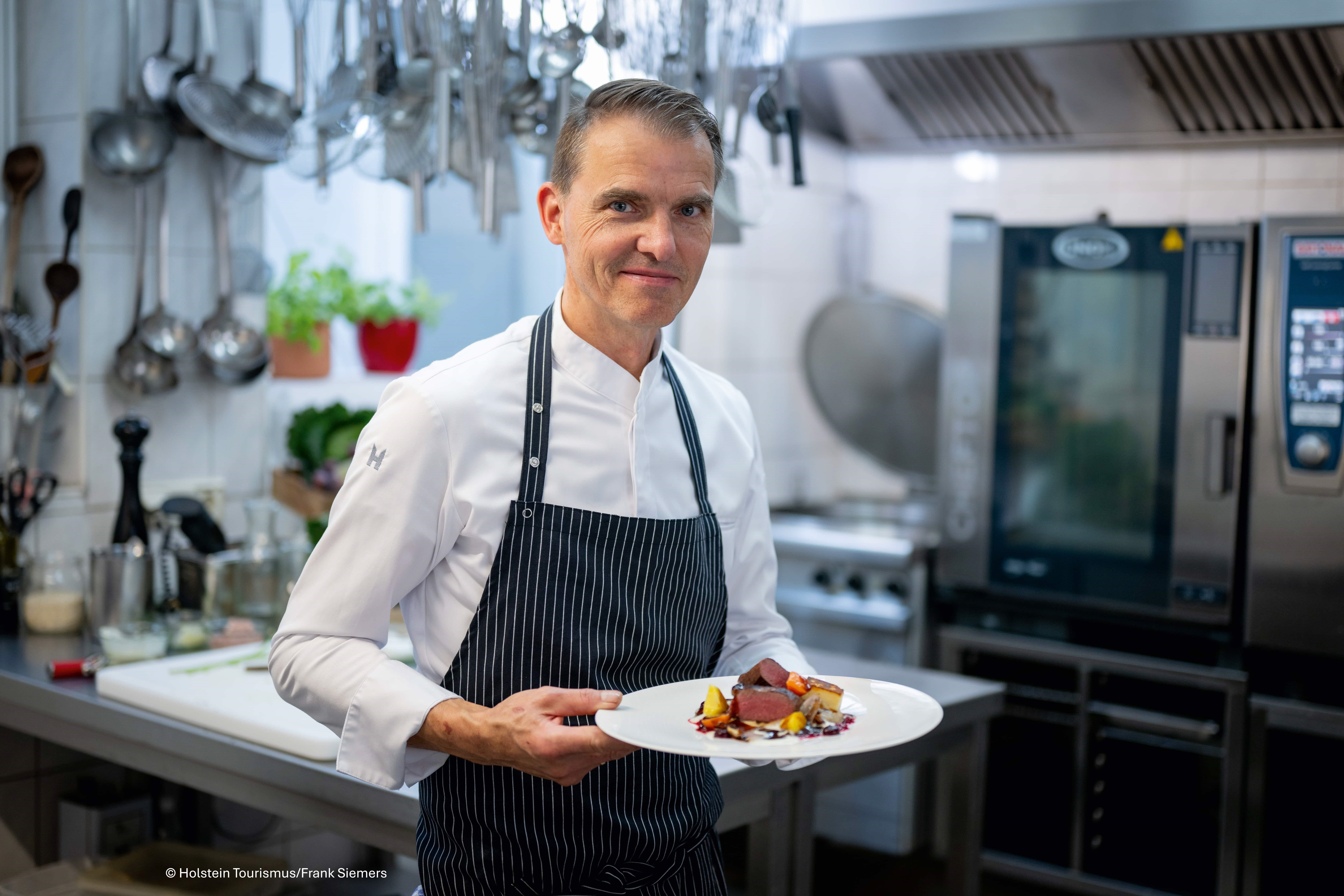 Koch in der Küche mit Teller in der Hand.