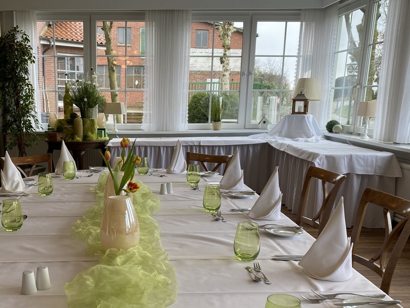 Kleiner Veranstaltungsraum mit eingedecktem Tisch mit grüner Deko.